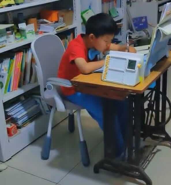 Cậu bé vừa đạp máy khâu, vừa làm bài tập về nhà